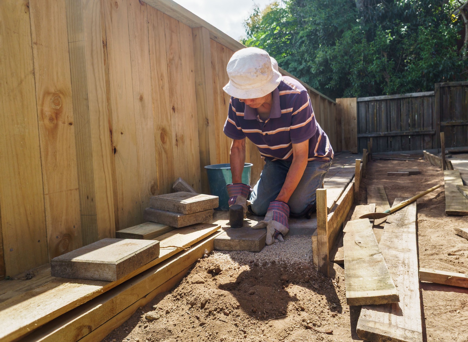 Man laying brick pavers in the backyard garden.